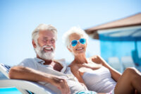 Cheerful senior couple lounging by a pool on sunny summer evening. Retired husband and wife going on vacation. Retirement hobby and leisure activity for elderly people. Generative AI.