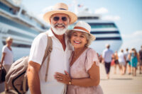 Attractive retired couple posing together wearing hats and smiling in front of the cruise ship on which they are going to celebrate their anniversary.